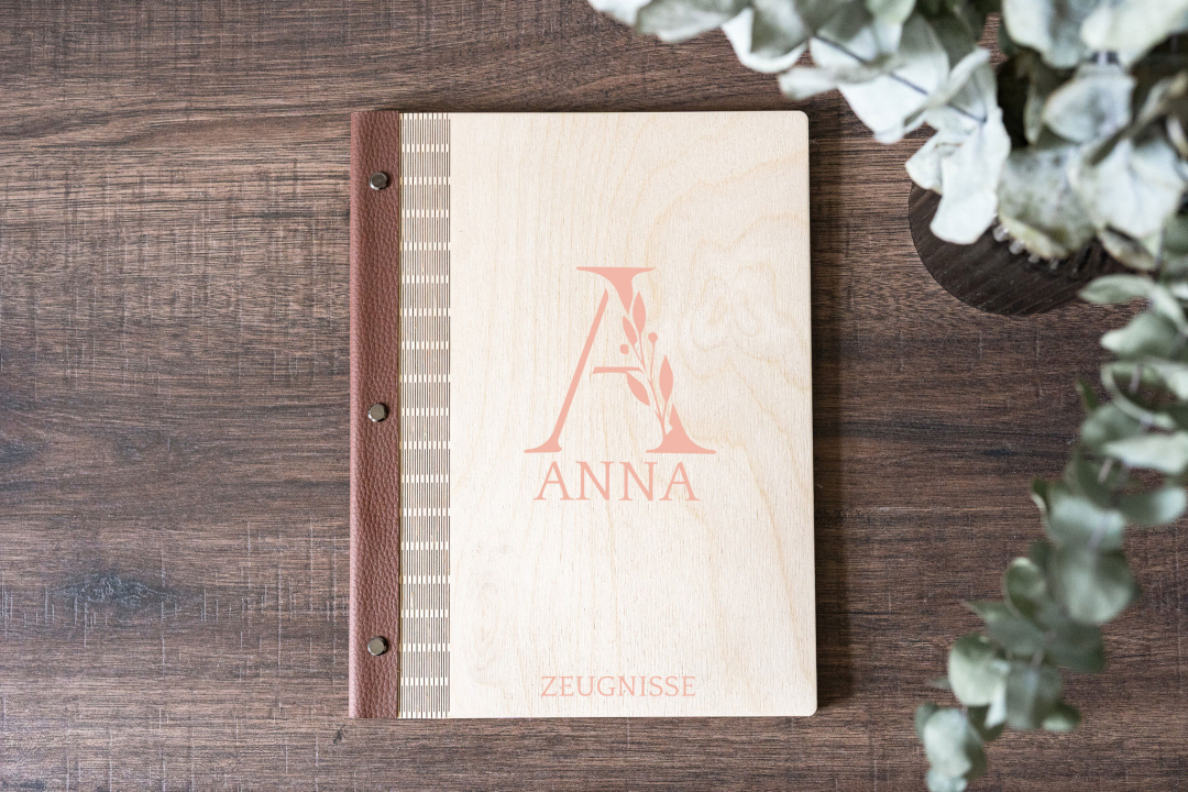 Zeugnismappe aus Birkensperrholz personalisiert mit Namen Anna und Monogramm, veganer Lederrücken, auf Holztisch mit Eukalyptuszweigen, Farbe altrosa